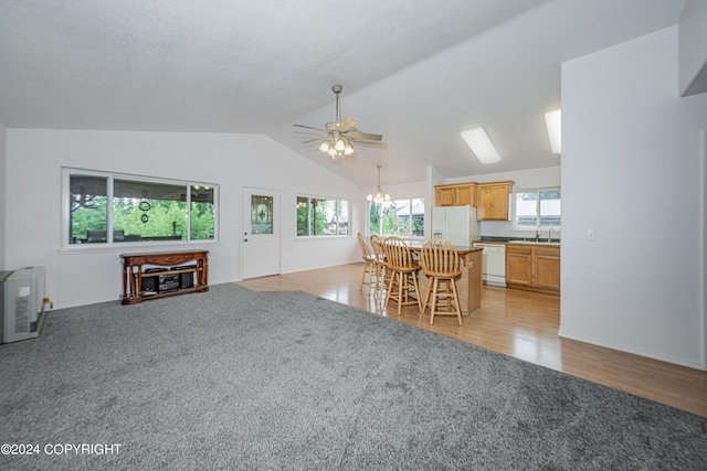 living room featuring light colored carpet, vaulted ceiling, light wood finished floors, and ceiling fan with notable chandelier