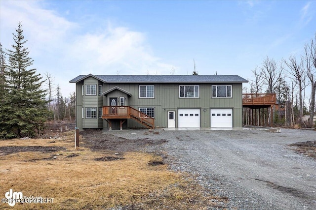 bi-level home featuring an attached garage, stairway, a deck, and gravel driveway