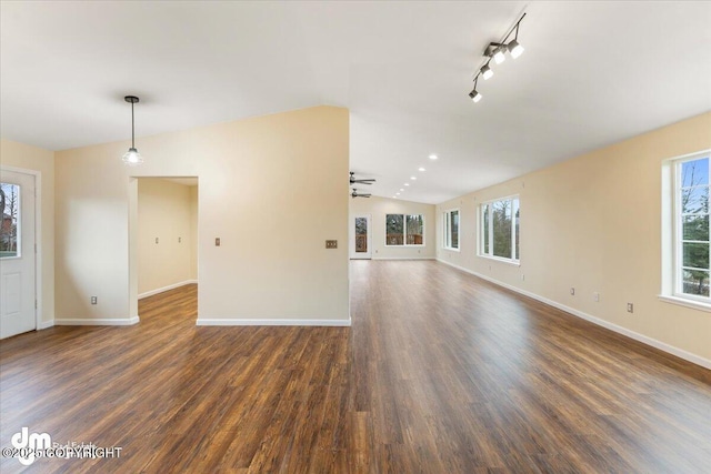 unfurnished living room featuring lofted ceiling, rail lighting, dark wood finished floors, and baseboards