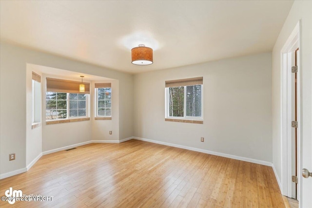 spare room with light wood-type flooring, visible vents, and baseboards