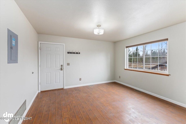 empty room featuring dark wood-style flooring, electric panel, visible vents, and baseboards