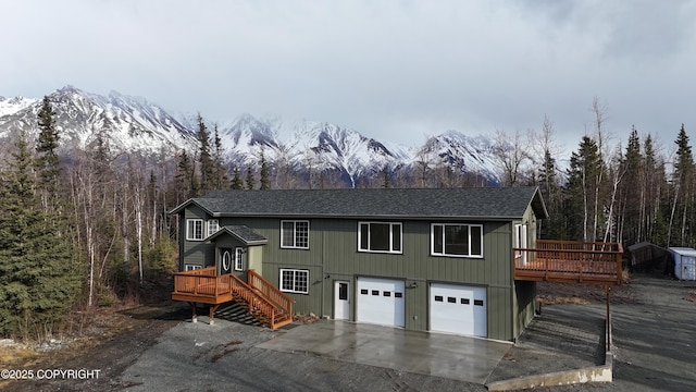 view of front of home with roof with shingles, a deck with mountain view, a garage, driveway, and a forest view