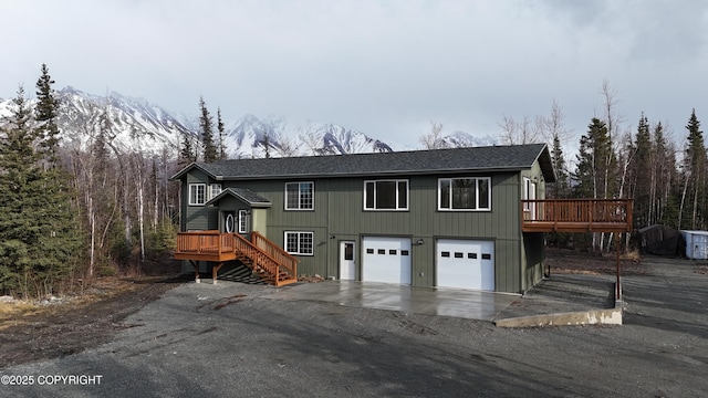 view of front facade with a deck with mountain view, driveway, roof with shingles, and an attached garage