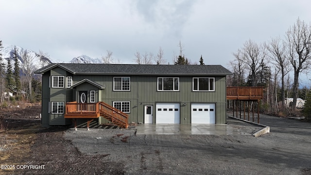 raised ranch featuring a garage, a shingled roof, stairway, aphalt driveway, and a deck with mountain view