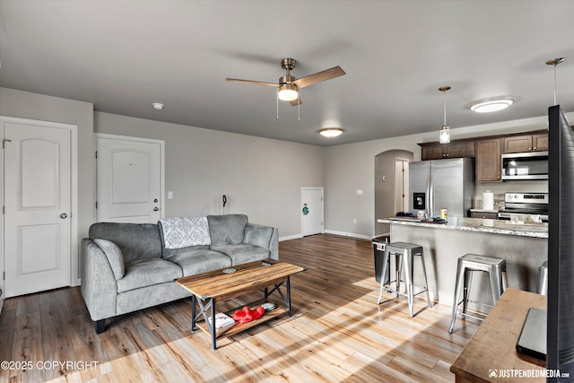 living area with arched walkways, ceiling fan, baseboards, and wood finished floors