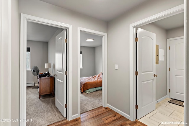 hall with light wood finished floors, a baseboard radiator, and baseboards