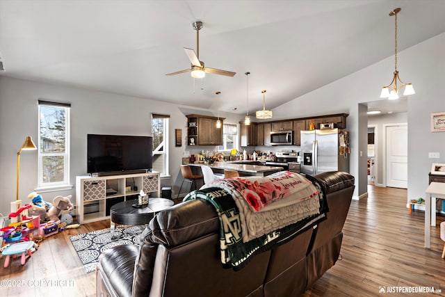 living area featuring a ceiling fan, baseboards, vaulted ceiling, and light wood finished floors