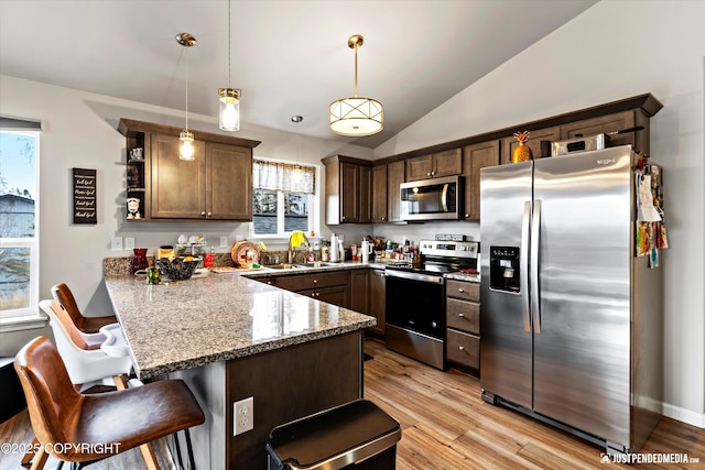 kitchen with a breakfast bar area, a peninsula, a sink, vaulted ceiling, and appliances with stainless steel finishes