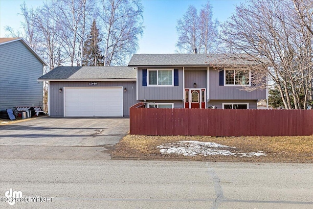 raised ranch featuring aphalt driveway, a garage, and a fenced front yard