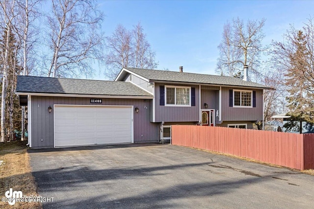 bi-level home with an attached garage, a shingled roof, driveway, and fence