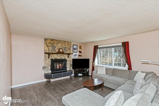 living room featuring a stone fireplace, wood finished floors, baseboards, and a textured ceiling