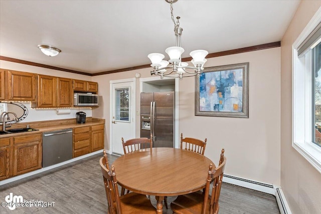 dining space with a baseboard heating unit, light wood-style flooring, ornamental molding, and a chandelier