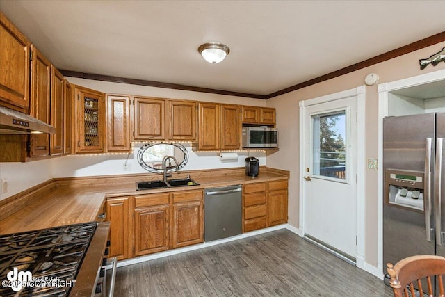 kitchen with brown cabinetry, dark wood-style floors, a sink, stainless steel appliances, and under cabinet range hood