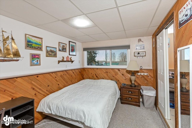 bedroom with a drop ceiling, wainscoting, wood walls, and carpet floors