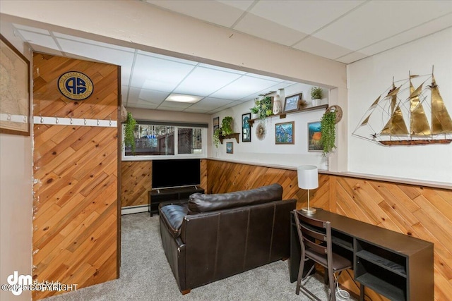 living area with a baseboard radiator, a paneled ceiling, carpet, and wooden walls