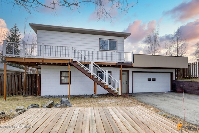 back of property at dusk featuring a deck, aphalt driveway, fence, stairway, and an attached garage