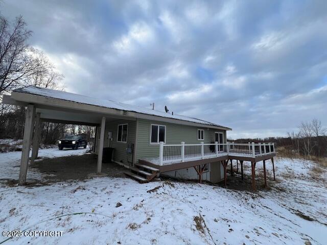 snow covered rear of property with an attached carport and a wooden deck