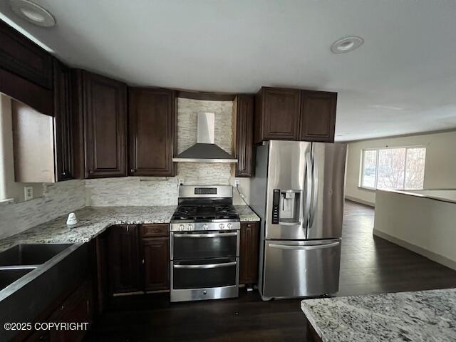 kitchen featuring tasteful backsplash, dark wood-style floors, wall chimney exhaust hood, stainless steel appliances, and dark brown cabinets