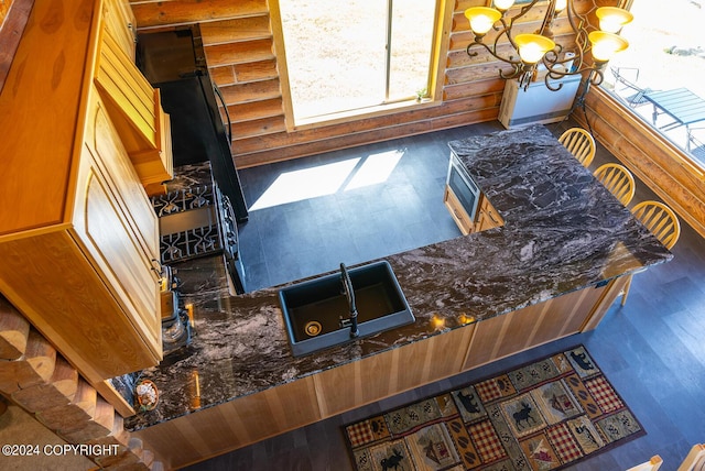 interior space featuring a chandelier, a sink, wood finished floors, dark stone counters, and rustic walls