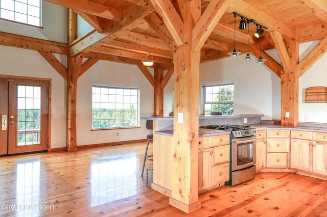 kitchen with light wood-style floors, beam ceiling, stainless steel gas stove, light brown cabinetry, and plenty of natural light