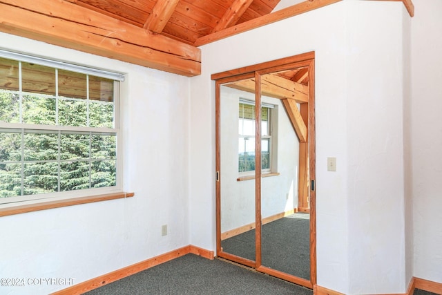 spare room featuring lofted ceiling with beams, wooden ceiling, baseboards, and dark carpet