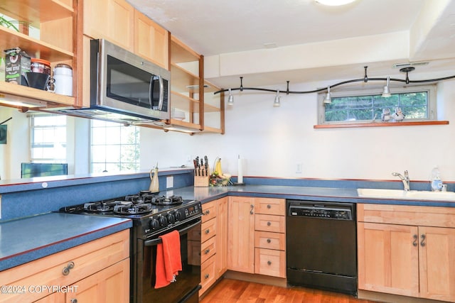 kitchen with a sink, light brown cabinetry, light wood-type flooring, black appliances, and dark countertops