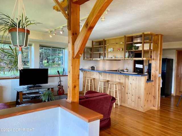 kitchen with a breakfast bar, wood finished floors, freestanding refrigerator, rail lighting, and open shelves