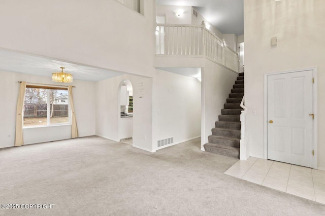 interior space featuring a notable chandelier, visible vents, a towering ceiling, carpet flooring, and stairs