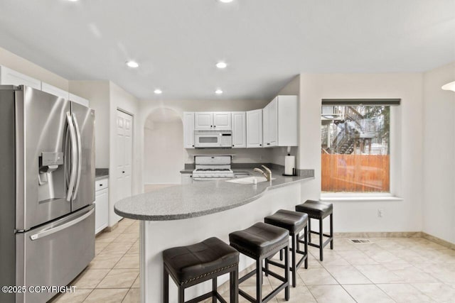 kitchen featuring arched walkways, white cabinetry, white appliances, a peninsula, and a kitchen breakfast bar