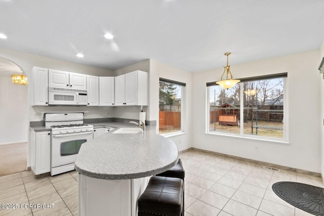 kitchen with white appliances, arched walkways, a peninsula, white cabinetry, and a sink