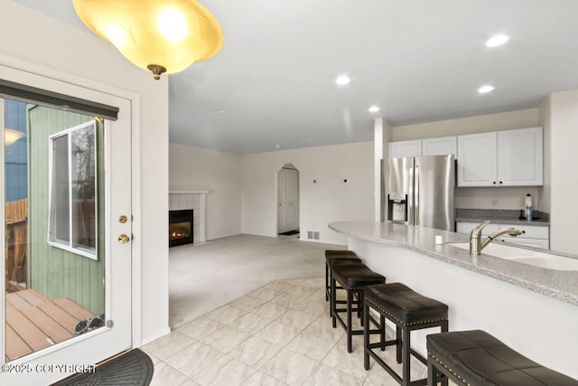 kitchen with a breakfast bar area, light colored carpet, a sink, stainless steel fridge with ice dispenser, and a tiled fireplace