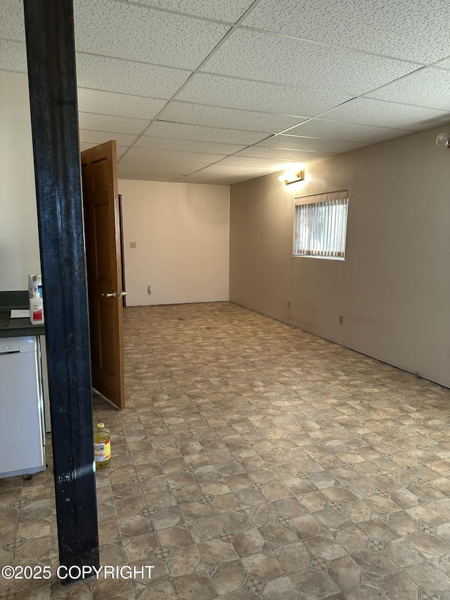 basement featuring a drop ceiling and refrigerator