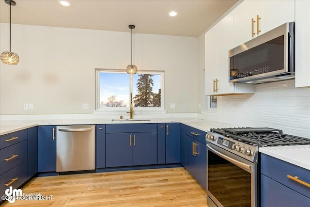 kitchen featuring light wood-style flooring, hanging light fixtures, stainless steel appliances, blue cabinetry, and a sink