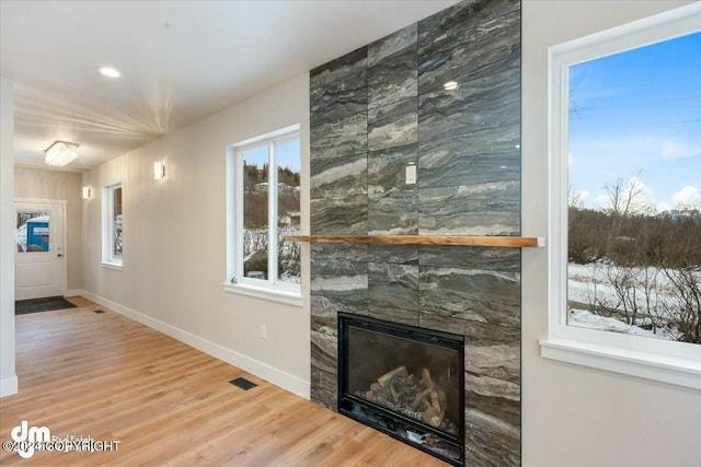 unfurnished living room with a large fireplace, visible vents, baseboards, and wood finished floors