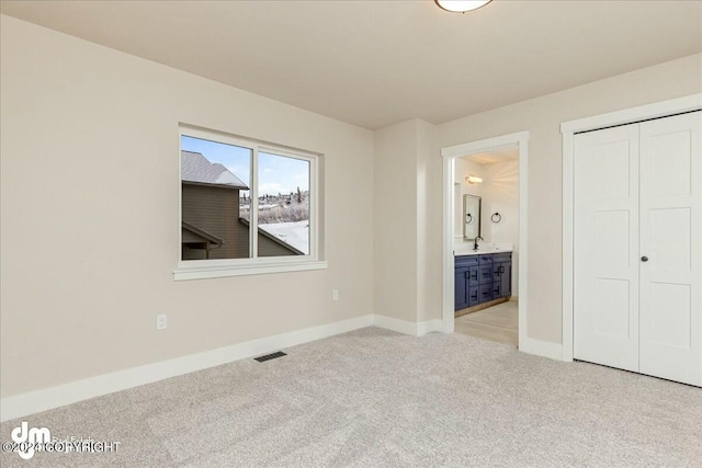 unfurnished bedroom featuring connected bathroom, light colored carpet, visible vents, baseboards, and a closet