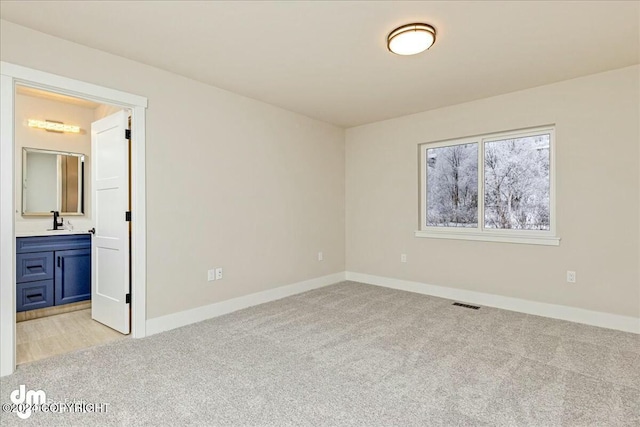 unfurnished bedroom featuring light carpet, a sink, visible vents, and baseboards