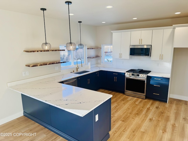 kitchen featuring light wood-style flooring, a sink, a peninsula, blue cabinetry, and stainless steel appliances