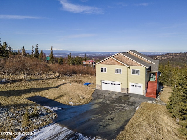 view of side of property featuring aphalt driveway, stone siding, and a garage