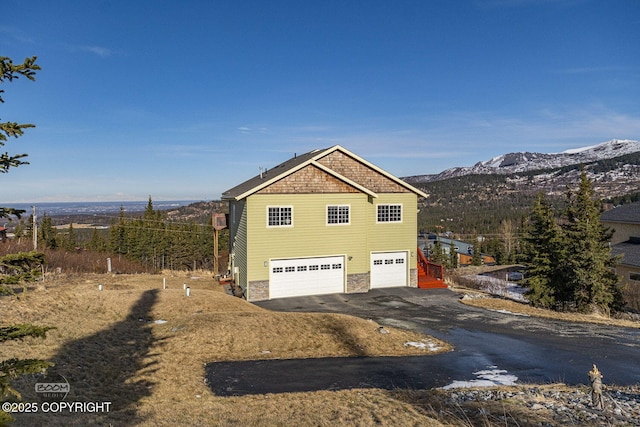 view of side of home featuring a garage, stone siding, driveway, and a mountain view