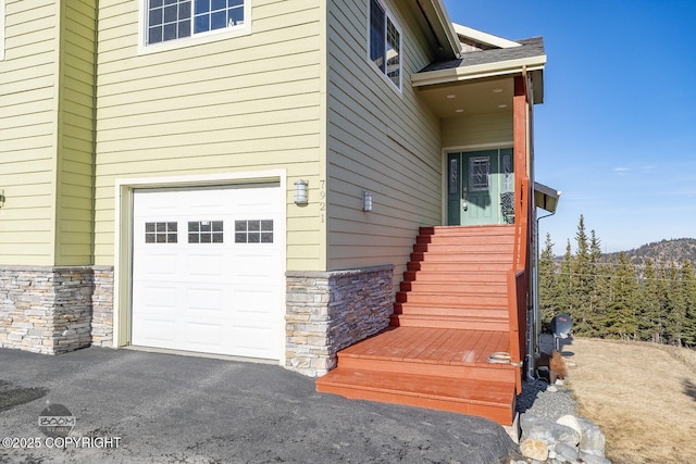 view of exterior entry with an attached garage and stone siding