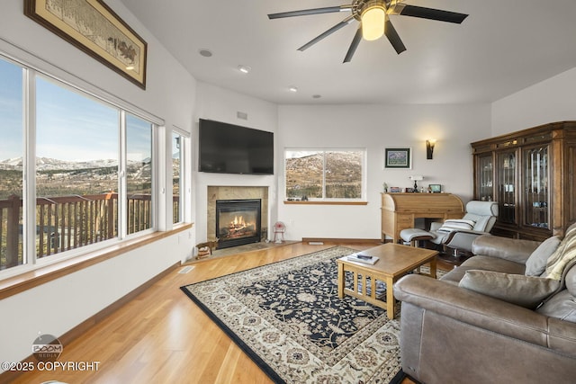 living room featuring ceiling fan, baseboards, a fireplace with flush hearth, and wood finished floors