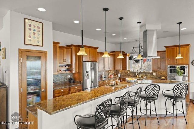 kitchen featuring brown cabinets, island exhaust hood, stainless steel appliances, a breakfast bar area, and a large island with sink