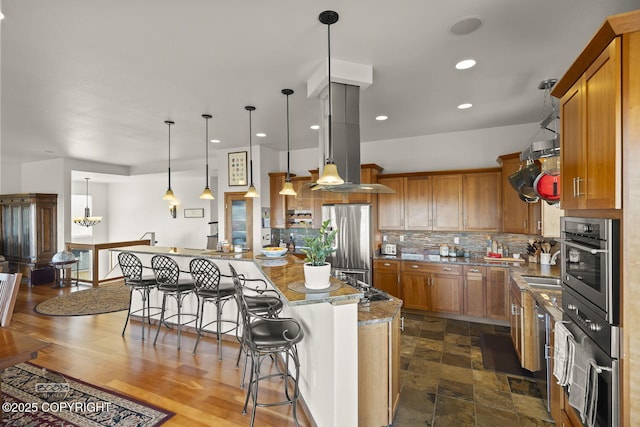 kitchen featuring decorative light fixtures, a kitchen breakfast bar, appliances with stainless steel finishes, decorative backsplash, and light stone countertops