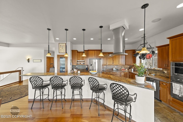 kitchen with brown cabinetry, a kitchen bar, appliances with stainless steel finishes, and island range hood