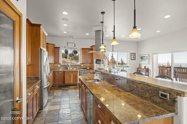 kitchen with beverage cooler, a sink, stone tile floors, decorative backsplash, and a large island with sink