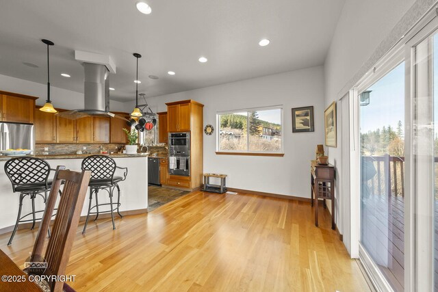 kitchen with light wood-style flooring, brown cabinetry, appliances with stainless steel finishes, and island range hood