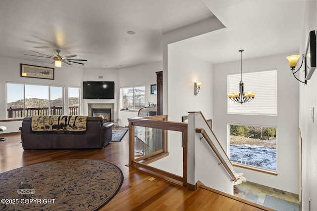 living room featuring a glass covered fireplace, ceiling fan with notable chandelier, wood finished floors, and a healthy amount of sunlight