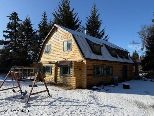 view of snowy exterior featuring roof with shingles, a playground, and a gambrel roof