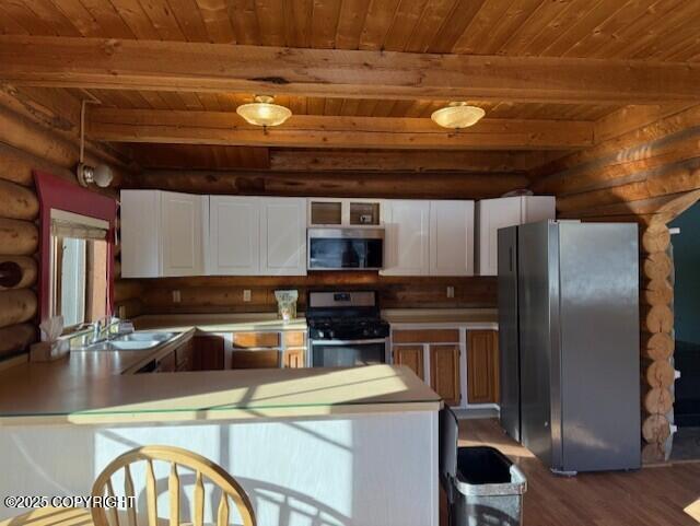 kitchen featuring stainless steel appliances, rustic walls, white cabinets, and beam ceiling