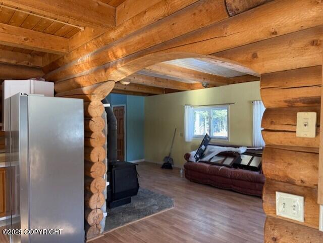 unfurnished living room featuring beam ceiling, wooden ceiling, wood finished floors, and a wood stove